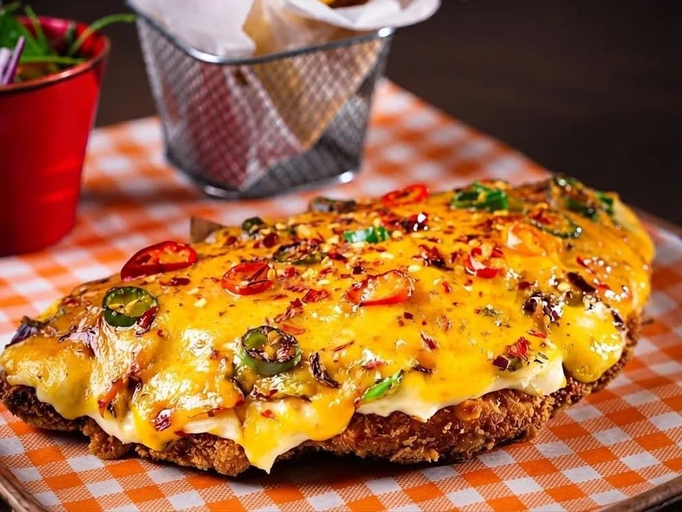 Hot Shot Parmo - a breaded chicken parmo under melted cheese with jalapenos and sliced chilli, a basket of chips behind, from Ashville Hot Chicken, JLT Dubai