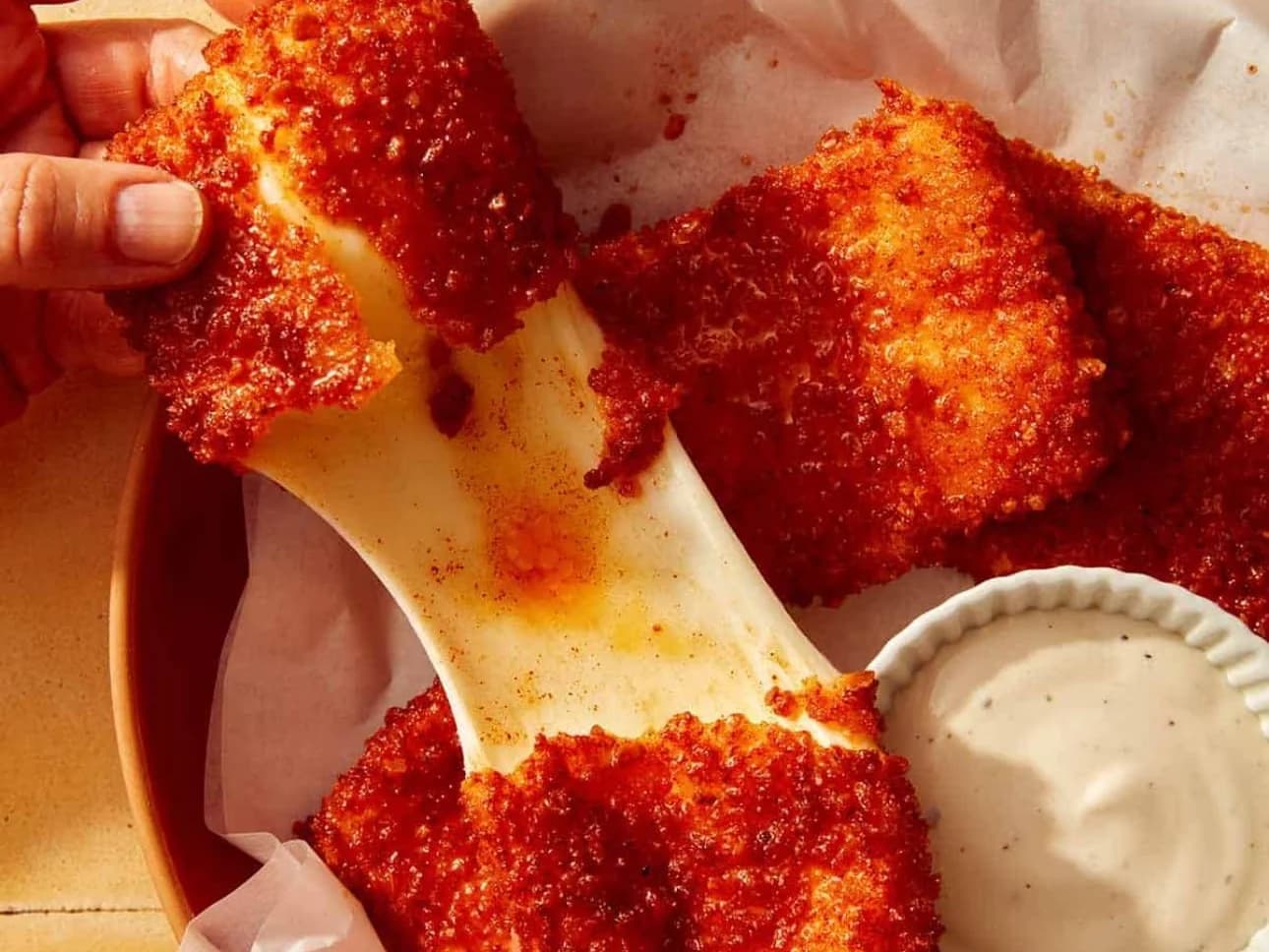 Nashville Hot Mozarella Sticks - crispy red-dusted mozzarella sticks pulled apart with a long cheese stretch, a pot of dip beside them, from Ashville Hot Chicken, JLT Dubai